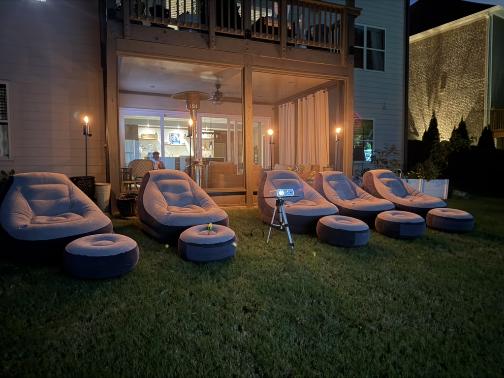 Cozy nighttime outdoor movie showing with projector and lounge chairs lit by torches