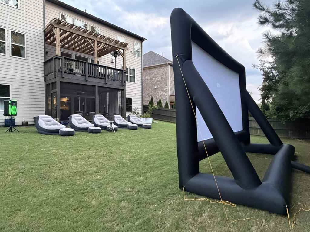 Side view of outdoor movie night setup with screen, loungers, and glowing speaker
