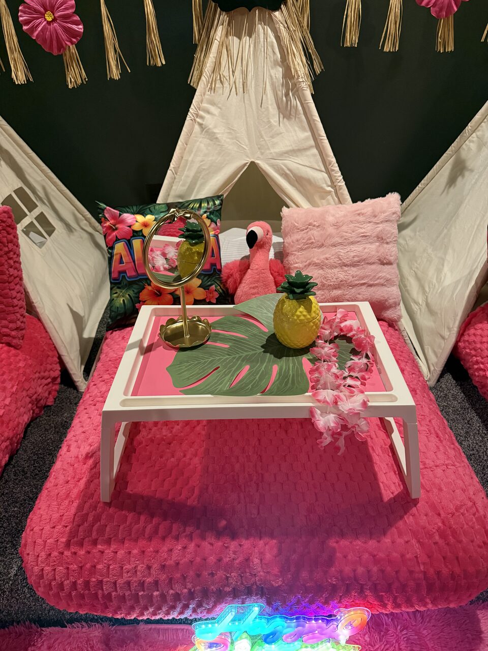 Close-up of a tropical pink teepee bed with flamingo, floral pillow, tray, mirror, and pineapple décor