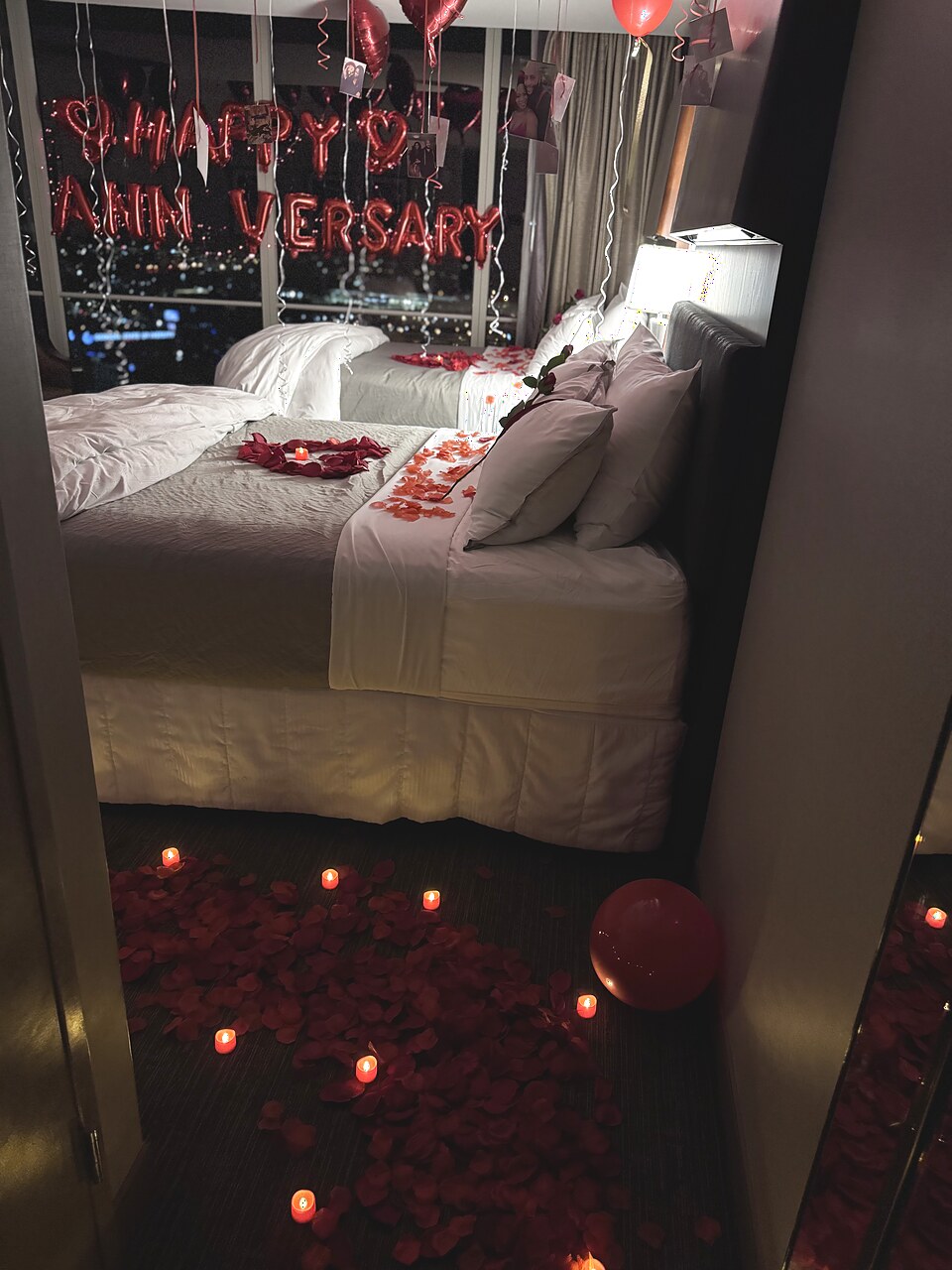Candlelit anniversary hotel room with rose petals and a city view