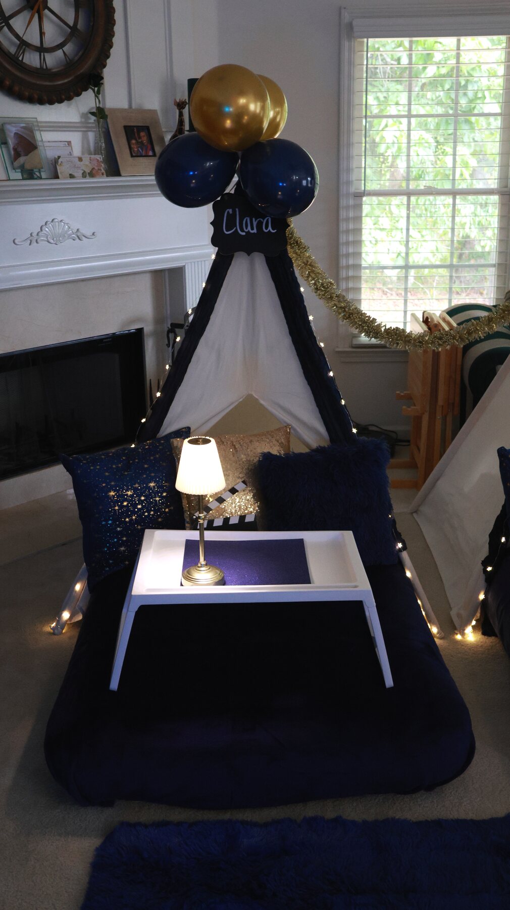 Close view of a navy-and-gold teepee with starry pillows, bedside lamp, tray, and string lights
